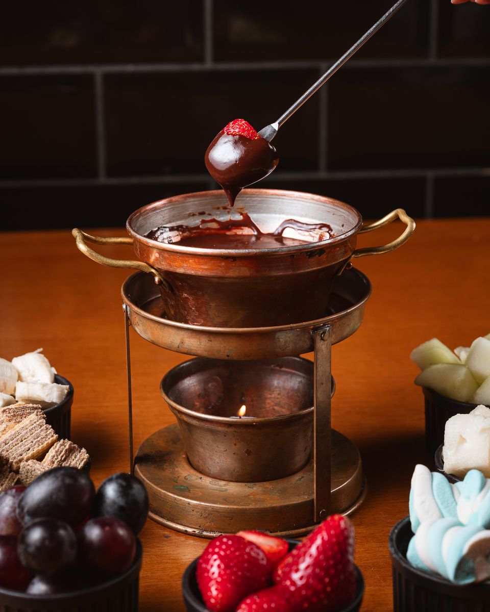 Morango mergulhado no fondue de chocolate, com frutas, waffer e marshmallow em volta